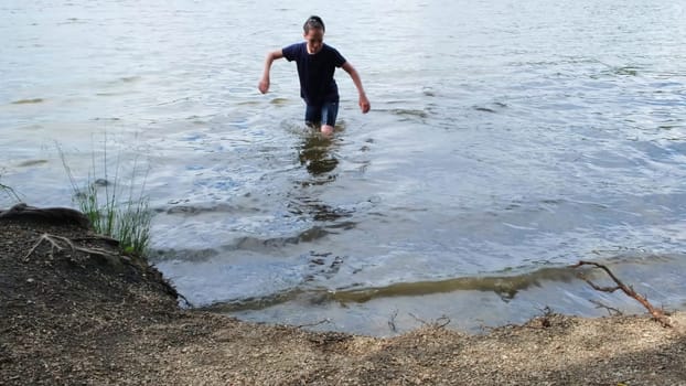 Boy went in water. Concept. Teenager went into water on lake on summer day. Boy went to bathe in clothes on sunny summer day.