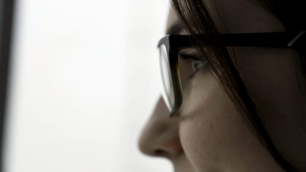 Extreme close up for young female face portrait in profile in black glasses on fuzzy, white background. Beautiful woman with her face in profile and short, dark hair