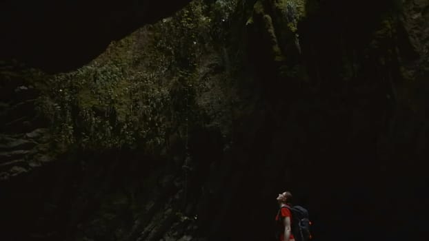 Woman at rocky cave in jungle. Creative. Hiking in rocky landscapes of wild jungle. Beautiful waterfalls and rocks in dark green forest.