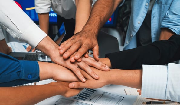 Group of diverse office worker join hand together in office room symbolize business synergy and strong productive teamwork in workplace. Cooperation and unity between business employee. Prudent