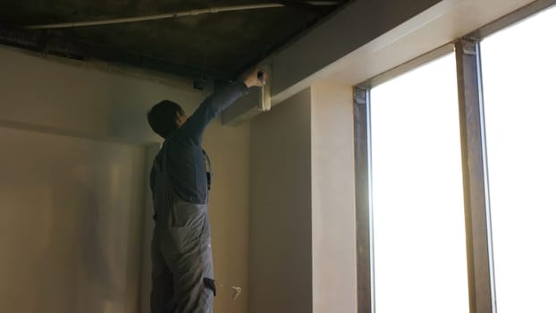 Painter working with paint roller to paint the wall of a room. Do it yourself concept. Man paints the wall with a roller at the window.