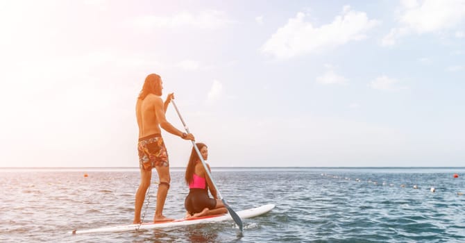 Sea woman and man on sup. Silhouette of happy young woman and man, surfing on SUP board, confident paddling through water surface. Idyllic sunset. Active lifestyle at sea or river