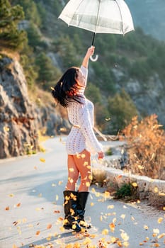 woman umbrella leaves , She holds him over her head, autumn leaves are falling out of him. Beautiful woman in a dress with an umbrella in the autumn park on the road in the mountains