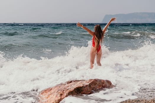 Woman travel sea. Young Happy woman in a long red dress posing on a beach near the sea on background of volcanic rocks, like in Iceland, sharing travel adventure journey