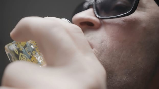 Close-up of man drinking vodka. Action. Man drinks glass while playing poker. Russian bandit in black glasses drinks vodka and plays cards.