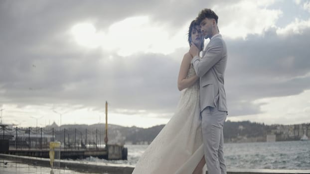 Street wedding photo session with urban architecture. Action.A glamorous and passionate couple in wedding costumes gently pose for a photographer next to big towers and the wind blowing their hair. High quality 4k footage