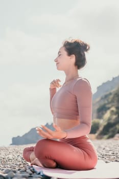 Young woman with long hair in white swimsuit and boho style braclets practicing outdoors on yoga mat by the sea on a sunset. Women's yoga fitness routine. Healthy lifestyle, harmony and meditation