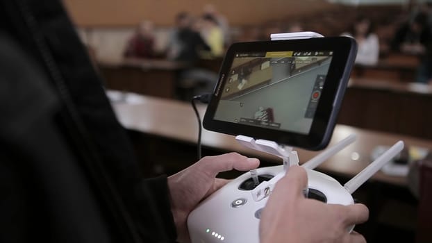 Close-up of man's hands with a remote control flying a small quadcopter toy indoors.