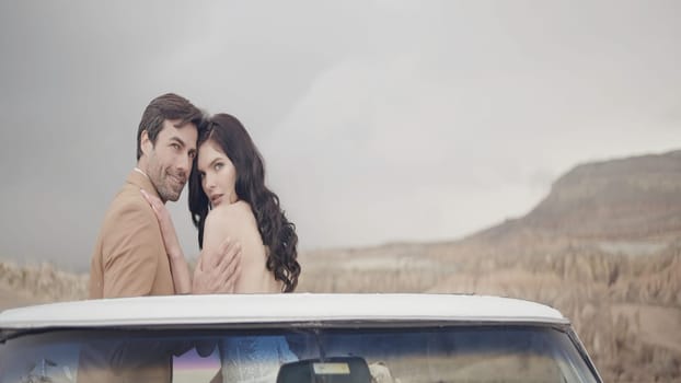 Beautiful couple of newlyweds in convertible. Action. Elegant couple in love on convertible. Beautiful newlyweds are sitting on convertible on background of sunny sky and rocks.