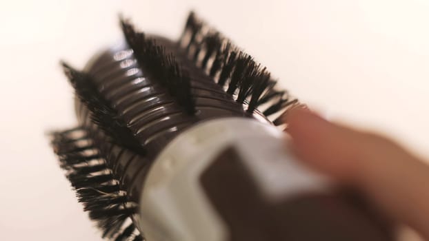 Girl holding a volumebrush for hair straightening isolated on white background. Woman hand pressing buttons of an automatic hair brush that is rotating into the both sides.