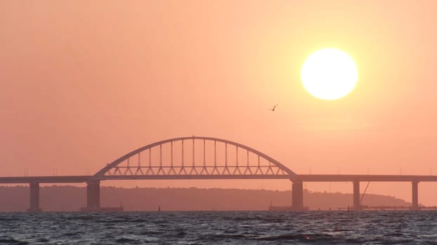 Amazing sunrise sky above the calm sea with ripples and white high bridge, beauty of nature. Golden sunrise above the horizon with time lapse effect.