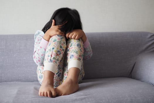 a upset child girl cover her face with hand .