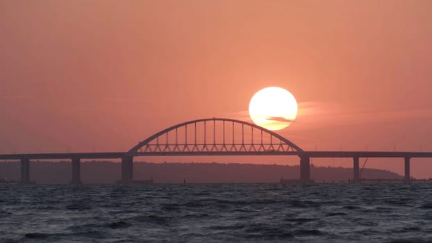 Stunning view of the beautiful sunset over the big river and the bridge, time lapse effect. Bright golden sun moving towards the horizon above the river.