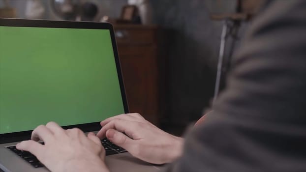 Close up rear view of young businessman hands typing on a laptop keyboard with a blank green editable screen. Man using laptop with chroma key.