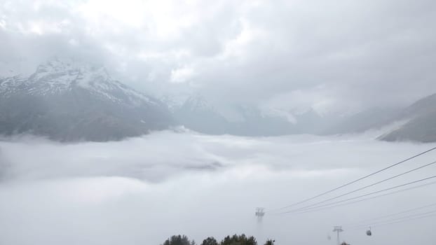 Beautiful mountain landscape with thick clouds. Creative. Rocky snowy mountain peaks with cloudy clouds. Low cumulus clouds in snowy mountains in autumn.