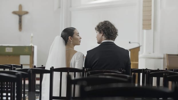 Bride and groom at the wedding ceremony in modern church. Action. Woman and man sitting together among empty seats