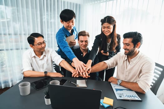 Group of diverse office worker join hand together in office room symbolize business synergy and strong productive teamwork in workplace. Cooperation and unity between business employee. Prudent