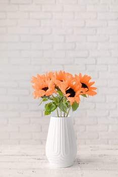 Color of the year 2024: Peach Fuzz. A bouquet of fresh sunflowers in a vase against the background of a white brick wall. copy space for text. Spring or autumn concept, yellow color