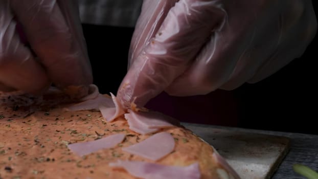Cooking pizza slow motion. Frame. Making pizza with cheese, tomato paste, sausage and mustard. The work of the cook. The cook arranges pieces of sausage and pizza with cheese and tomato paste. Full process of sprinkle milled cheese, slice meat and warp dough. Vertical look.