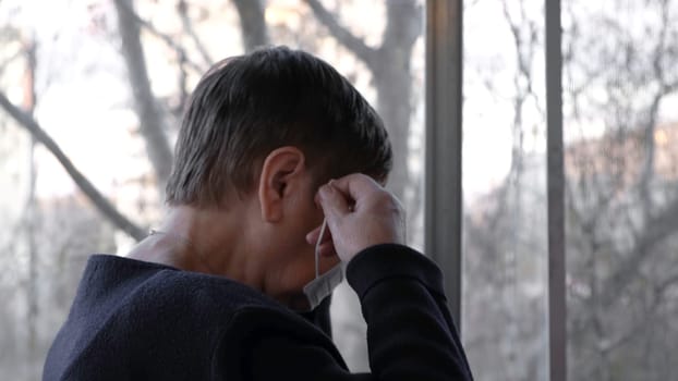 Elderly woman puts on protective mask indoors. Concept. During virus epidemic older people should take better care of themselves and use protective equipment.