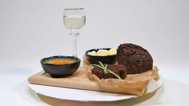 Fresh red caviar with basil and butter on bread in studio. Bred with red caviar with wine glasses on background. Cold Russian vodka with ice and small snacks sandwiches with butter and red salmon caviar on an old wooden table in rustic style, selective focus