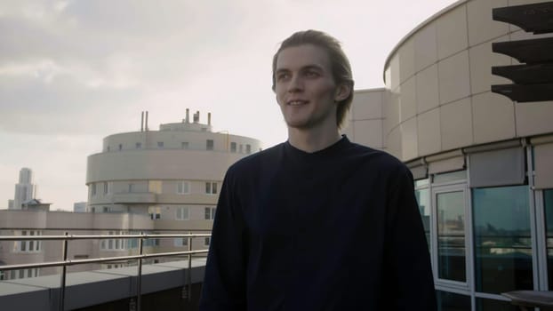 Portrait of a man in black clothes on the outdoor terrace. Stock. Man on a balcony smiling and then worried walking away