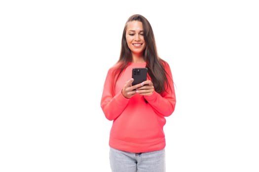 close-up of a young slender beautiful European lady with dark long straight hair in a pink sweater typing a message on a smartphone.