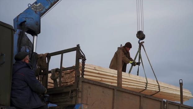 Men unload crane with wood. Clip. Workers unloading wood with crane. Crane with wooden beams is lowered into truck with worker.