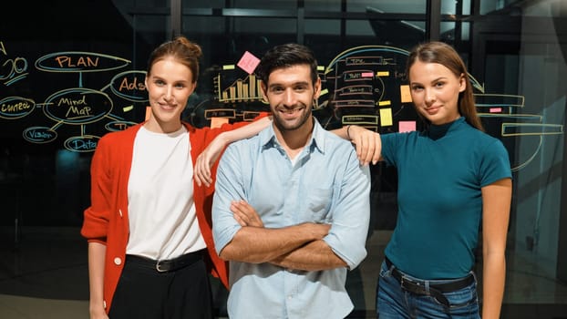 Professional business team crossing arms while standing together at glass wall. Group of businesspeople standing with arm folded while smiling at camera with confident in night office. Tracery