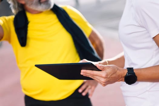 unrecognizable senior sports man and personal trainer planning training with a tablet, concept of healthy and active lifestyle in middle age