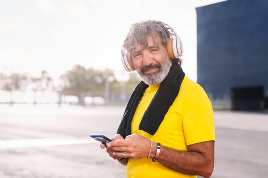 senior sports man listening to music from cell phone with headphones, concept of active lifestyle in middle age, copy space for text