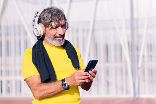 senior sports man listening to music from mobile phone with headphones, concept of active lifestyle in middle age, copy space for text