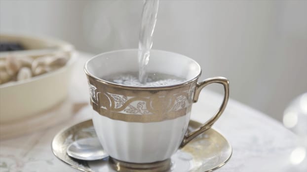 Close up of porcelain mug of white and golden colors standing on the table with hot tea. Hot water is poured into a ceramic cup on the table.