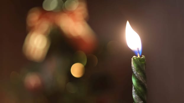 Close-up of lighted and extinction Christmas candle against the blurred Christmas tree silhouette with lights and decorations. Christmas mood