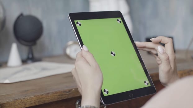 Side view of a woman holding tablet pc with green screen on wooden table background. Close up of a girl using Ipad with chroma key.