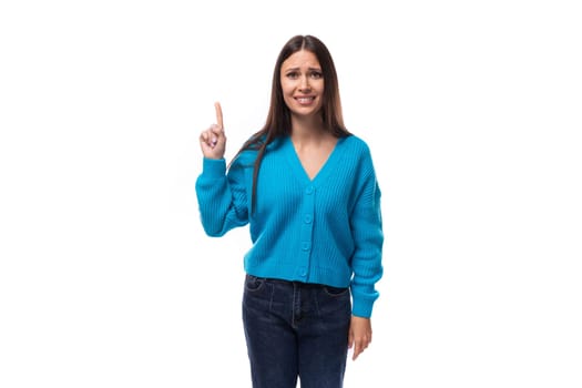 young pretty european brunette woman dressed in a blue cardigan points her fingers at the advertising space.