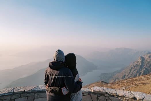 Man and woman are hugging on a mountain looking at the Bay of Kotor in the fog. Montenegro. Back view. High quality photo