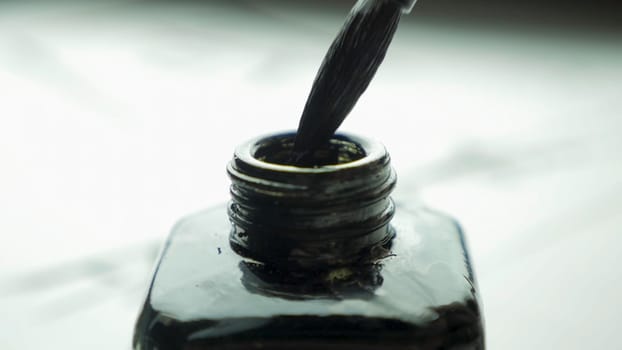 Female hand dunks brush in a jar of ink for drawing close up. Chinese Old-fashioned Paint Brushes with Selective Focus. Detail of a chinese brush while drawing a line in light back 4K