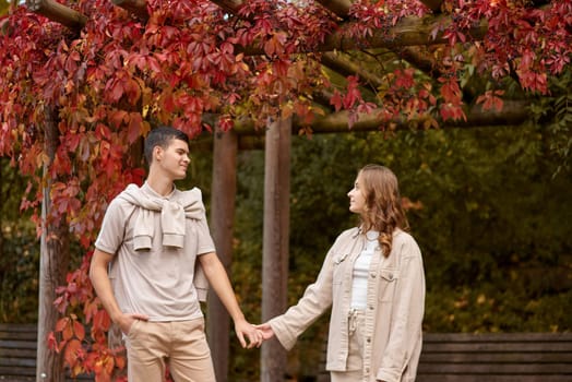 Young couple in love walking in the autumn park holding hands looking in the sunset. Closeup of loving couple holding hands while walking at sunset. The hands of the male and female lovers who hold hands walk forward high with blurred background