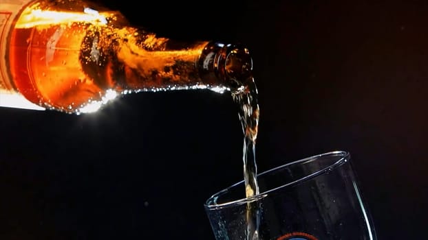 Close up of pouring beer from the glass brown bottle into the glass. Video. Pouring alcoholic drink isolated on black background, concept of party