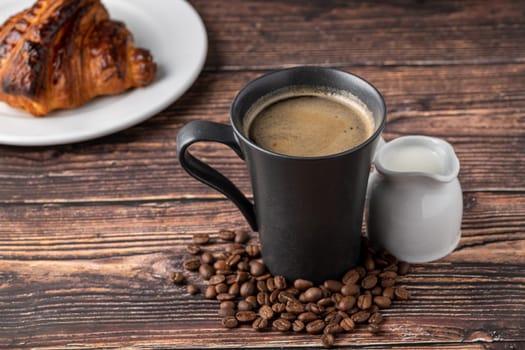 Relaxing americano coffee in black porcelain cup with milk on wooden table