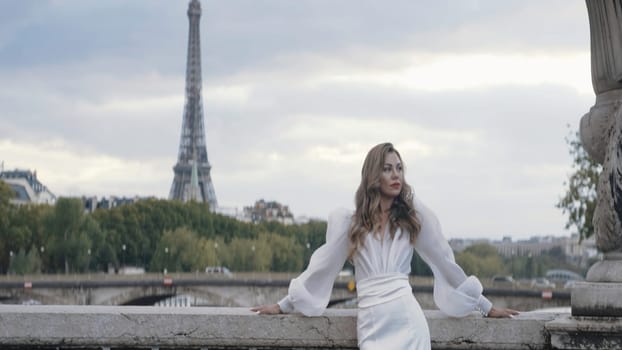 Gorgeous woman in dress on background of Paris. Action. Woman in elegant white dress on background of Eiffel Tower. Beautiful elegant woman in dress on street of Paris.