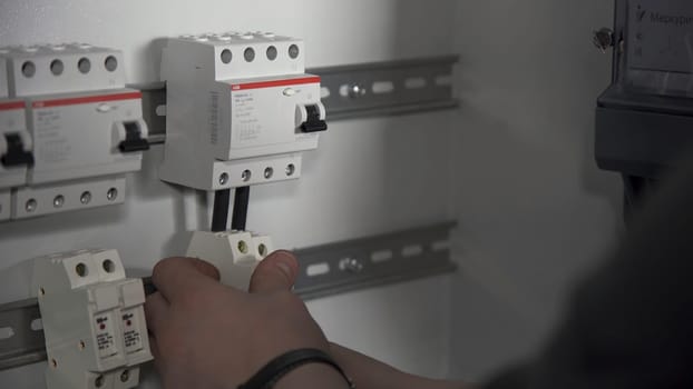 Close up of electrical switchboard with automats and wires. Man hands performing installation of electric shield.