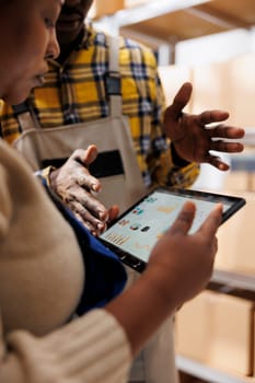 Inventory analyst explaining warehouse employee data on tablet screen. African american industrial storehouse manager holding portable device and analyzing stock supply analytics