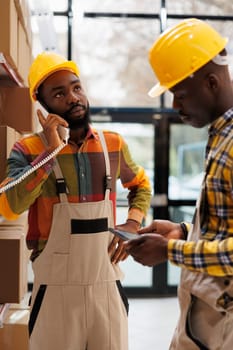 Warehouse manager listening to supervisor explaining inventory management on landline phone. All black storehouse workers team discussing products stock supply with distribution operator on telephone