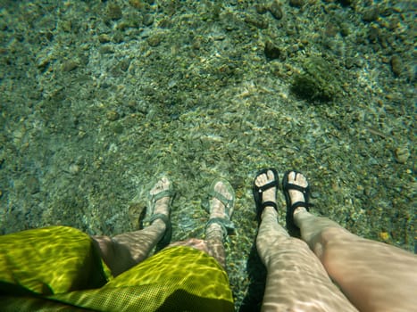 Two individuals stand in clear water, showcasing the rocky riverbed beneath them.