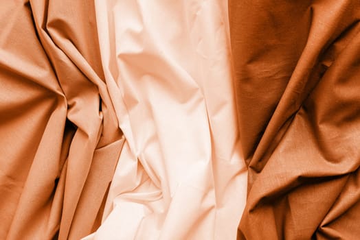 Color of the year 2024: Peach Fuzz. Closeup of rippled white, gray and brown silk fabric. Abstract texture background