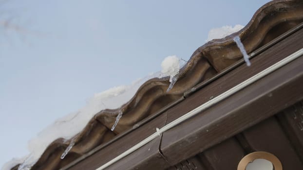 Close-up of dripping icicles on roof of house. Action. Bottom view of dripping icicles from cornice of house. Spring icicles dripping on background of sky.