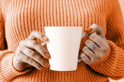 Color of the year 2024: Peach Fuzz. closeup woman hands in sweater holding white mug for mockup design