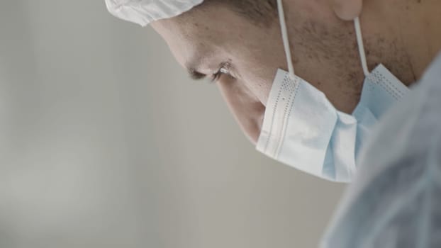 Caucasian male healthcare professional in a hospital operating theatre wearing a surgical cap and mask. Action. Surgeon during procedure
